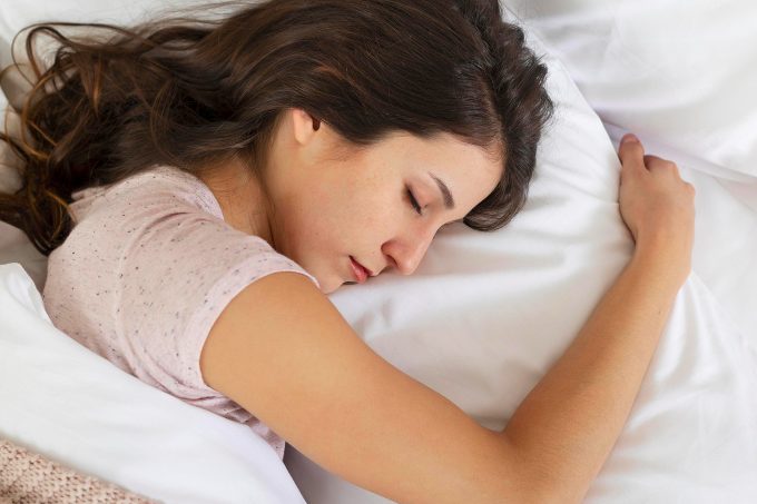 Eine schlafende Frau liegt mit dem Kopf auf einem Kissen in einem Bett.