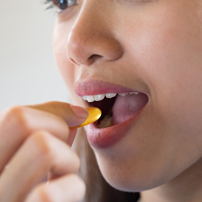 Frau nimmt eine gelbe Kapsel aus der Hand und führt sie zum Mund.